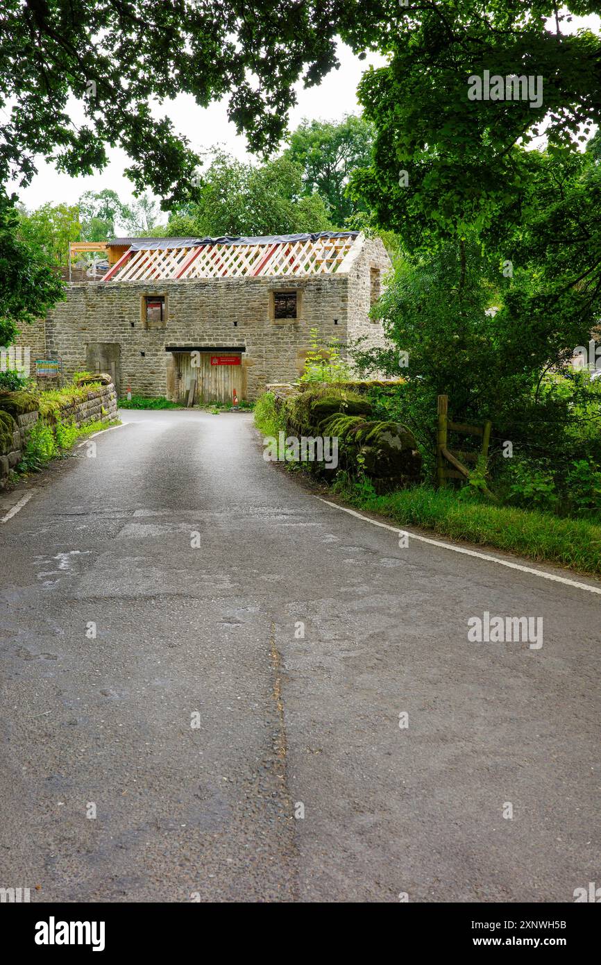 Eine ruhige Landstraße führt zu einem charmanten, teilweise renovierten Steingebäude, umgeben von üppigem Grün. Stockfoto