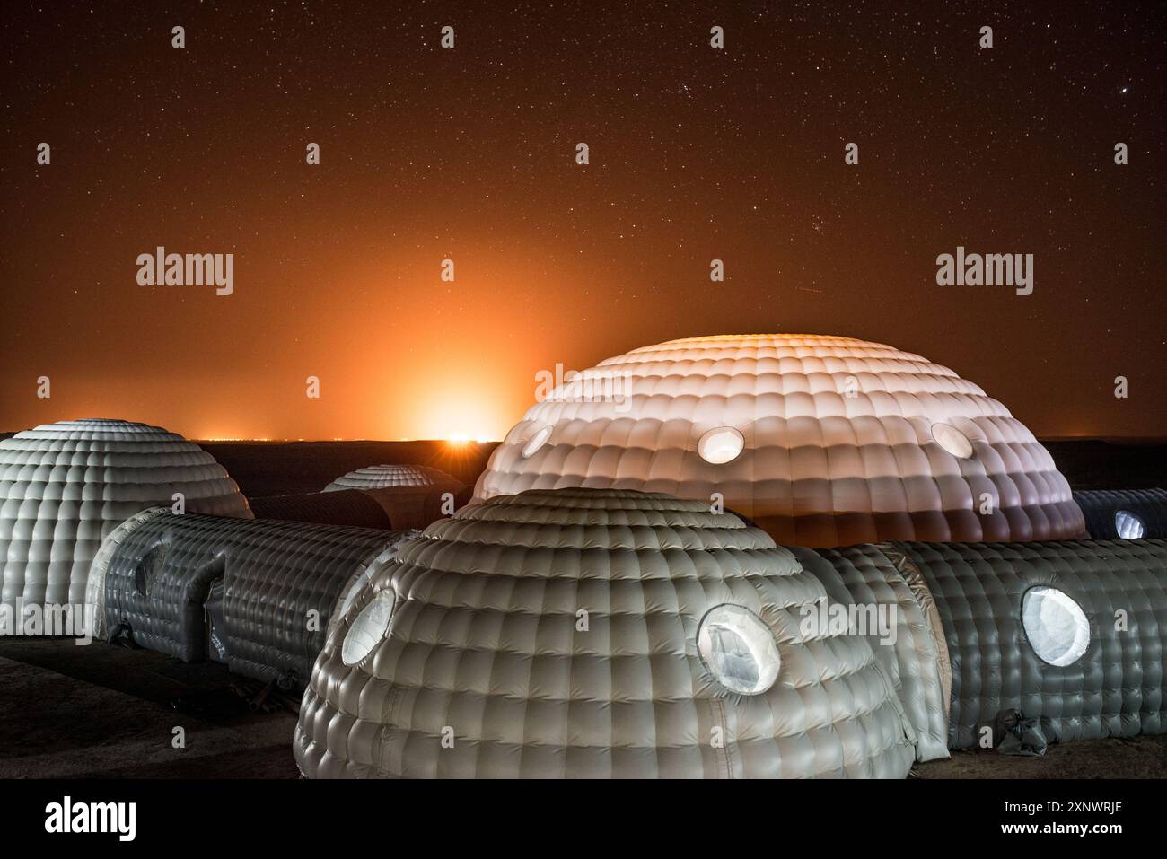 Eine faszinierende Szene mit futuristischen Kuppelbauten unter einem Sternenhimmel mit leuchtendem Horizont. Dieses Bild kann neue Anfänge, Innovationen und Entdeckungen symbolisieren und Gefühle des Staunens und der Neugier wecken. Stockfoto
