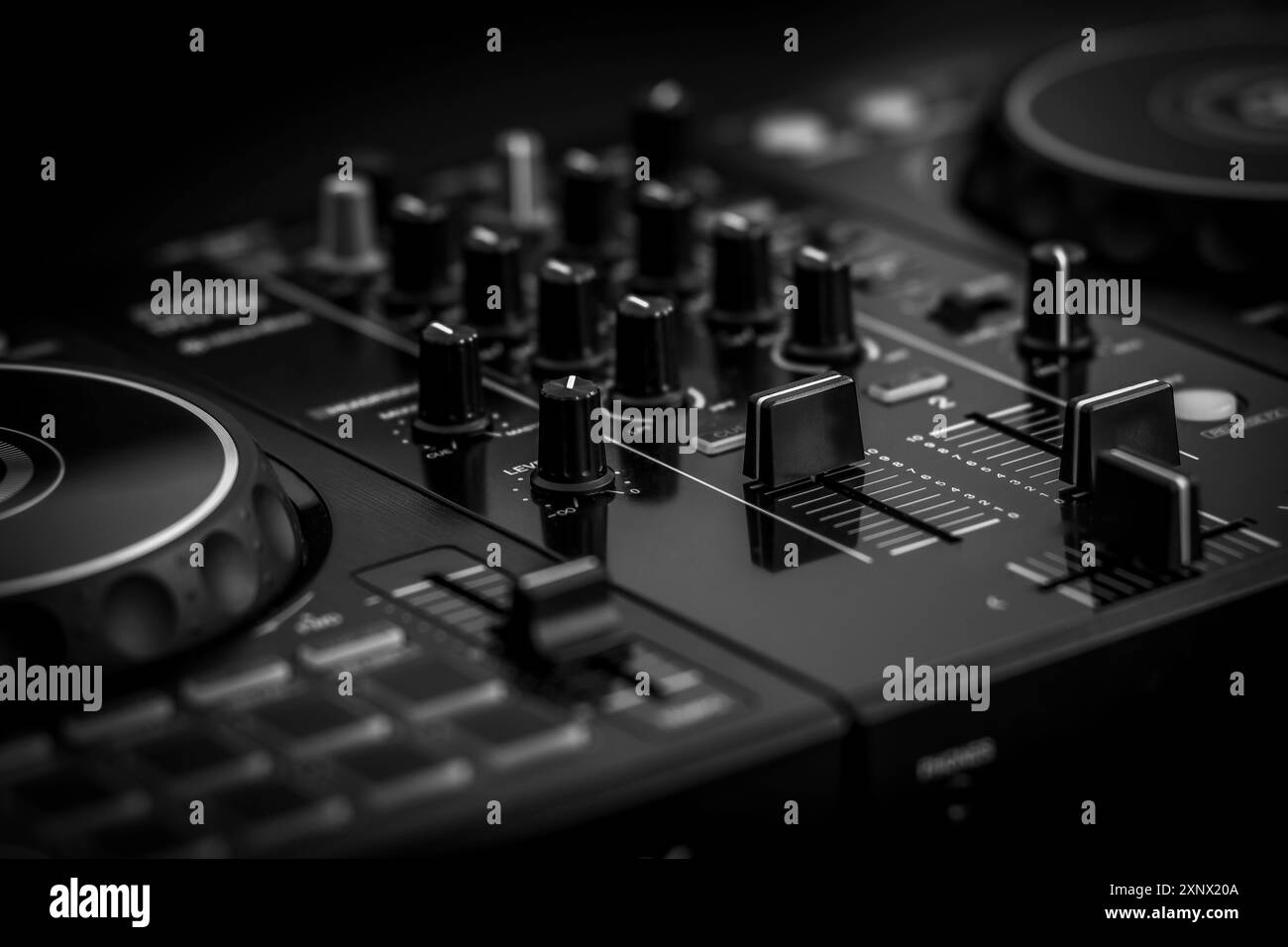 Nahaufnahme eines schwarzen DJ-Mischpults mit zahlreichen Reglern und Fadern, aufgenommen in Schwarzweiß-Einstellung, Mixer-dj-Audio Stockfoto