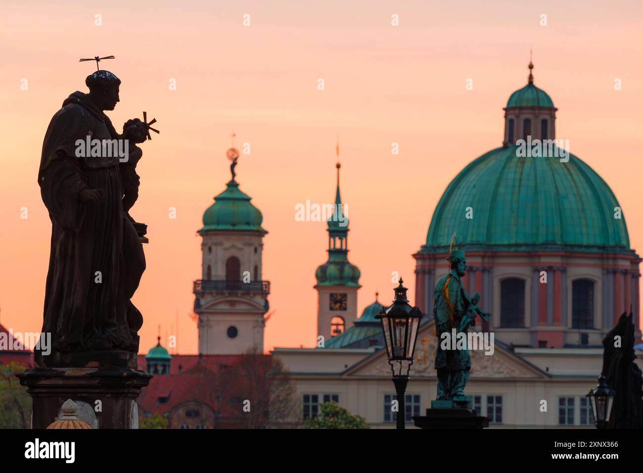 Statue an der Karlsbrücke mit einer Kuppel des hl. Franz von Assisi im Hintergrund bei Sonnenaufgang, UNESCO-Weltkulturerbe, Prag Stockfoto