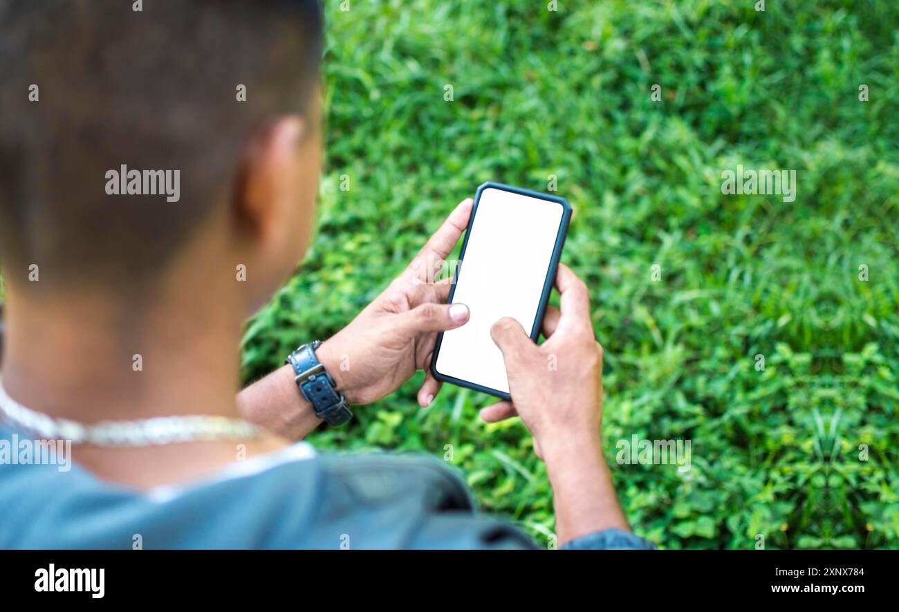 Ansicht eines Mannes, der auf dem Gras das Telefon überprüft. Nahaufnahme einer Person, die draußen telefoniert Stockfoto