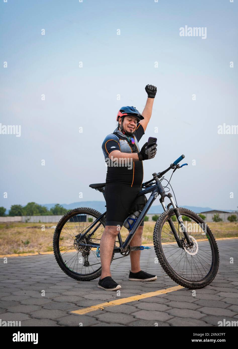 Professioneller Radfahrer, der glücklich auf das Handy auf der Straße schaut. Radfahrer im Sportanzug mit Handy glücklich auf der Straße Stockfoto