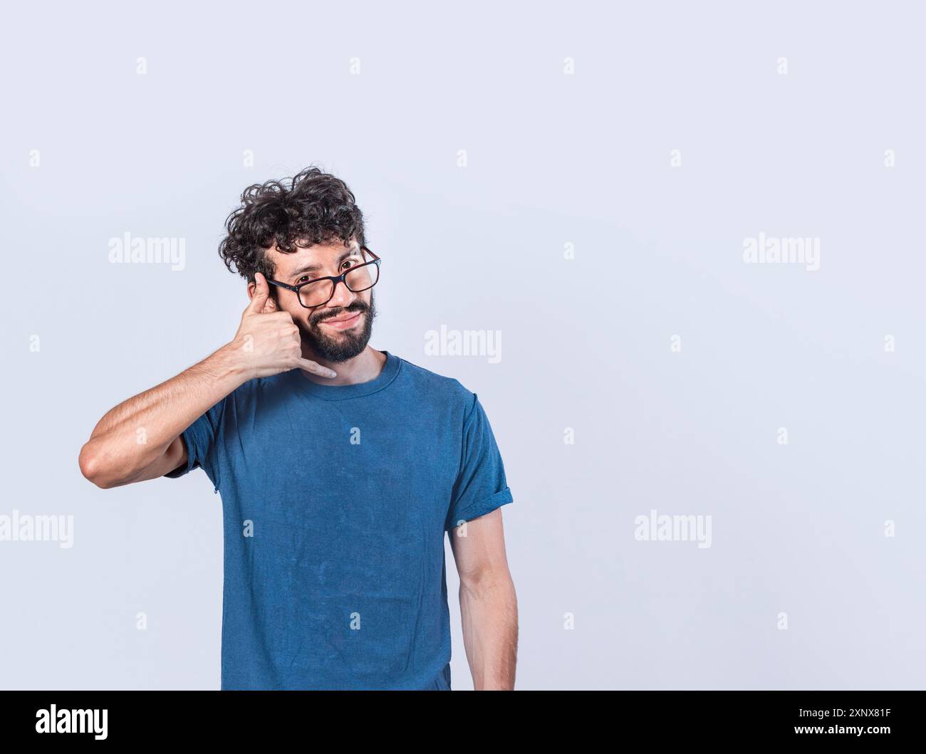 Attraktiver kaukasischer junger Mann in lässiger Kleidung imitiert Telefongespräche, hält die Hand in Ohr, als würde er ein Handy halten Stockfoto