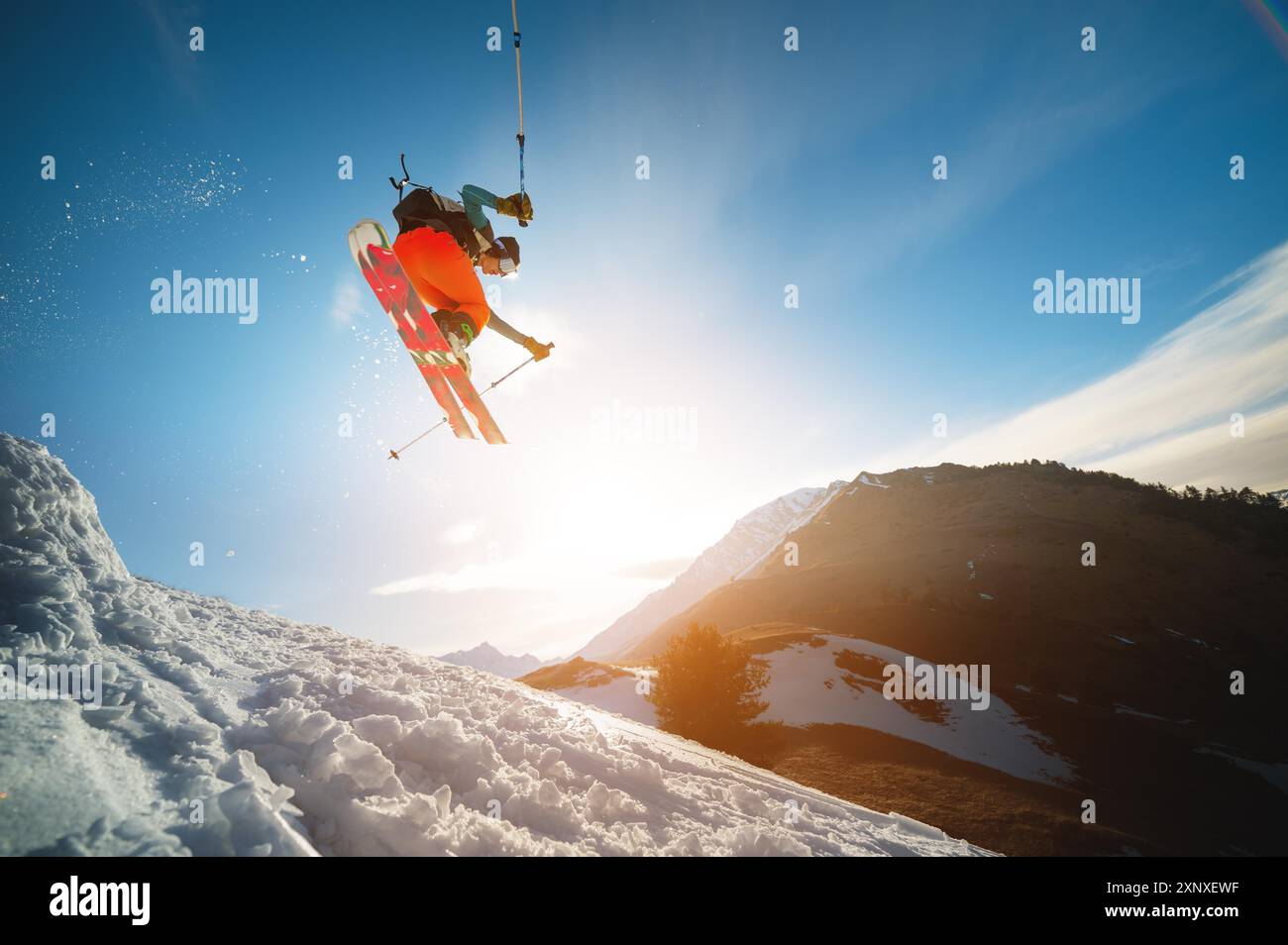 Mann Skier im Flug, nachdem er im Frühjahr von einem Kicker vor der Kulisse der Berge und des blauen Himmels gesprungen ist. Nahaufnahme Weitwinkel. Das Konzept von Stockfoto