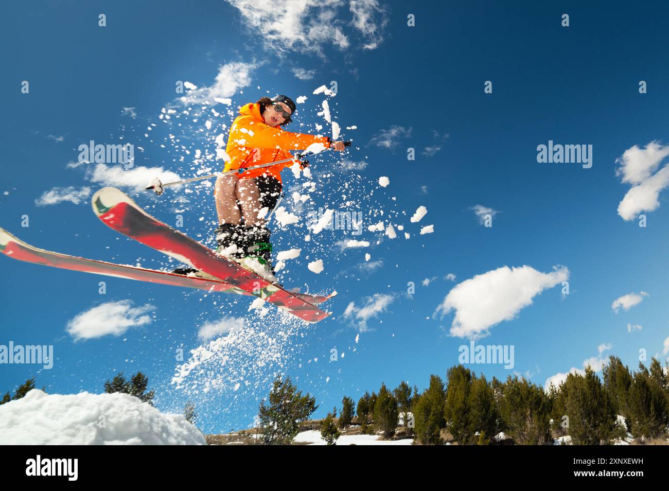 Mann Skier im Flug, nachdem er im Frühjahr von einem Kicker vor der Kulisse der Berge und des blauen Himmels gesprungen ist. Nahaufnahme Weitwinkel. Das Konzept von Stockfoto