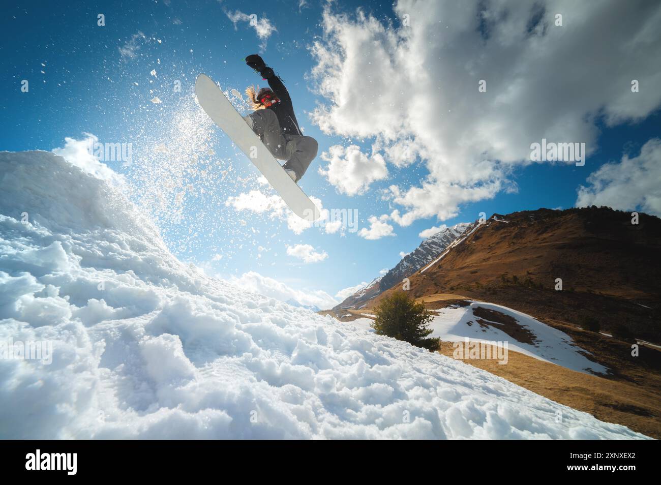 Extremer Wintersport. Eine junge Profi-Snowboarderin reitet eine Halfpipe. Springt von einem Halfpipe-Trampolin in der Sonne, führt Tricks und Wendungen durch Stockfoto