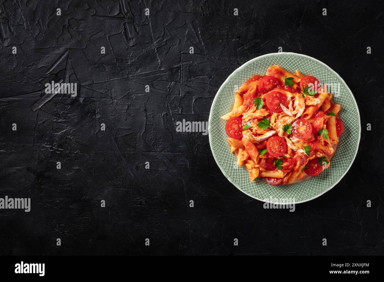 Pasta mit roter Sauce. Penne mit Huhn, Tomaten und Petersilienblättern, von oben mit einem Platz für Text, auf einem dunklen Hintergrund geschossen Stockfoto