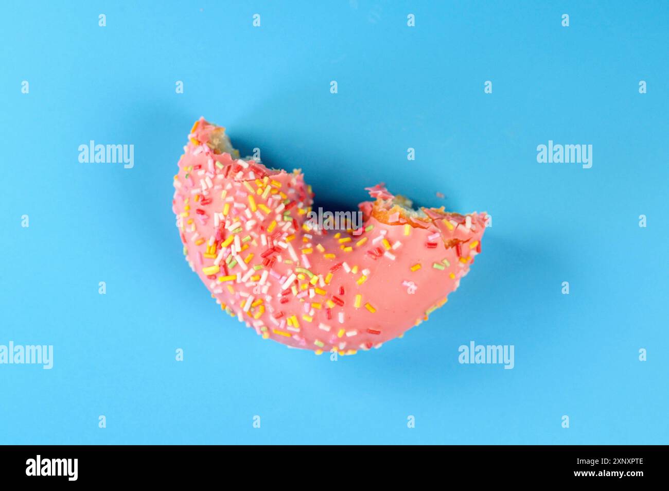 Rosafarbener, mattierter Donut mit bunten Streuseln, ohne Biss. Auf blauem Hintergrund Stockfoto