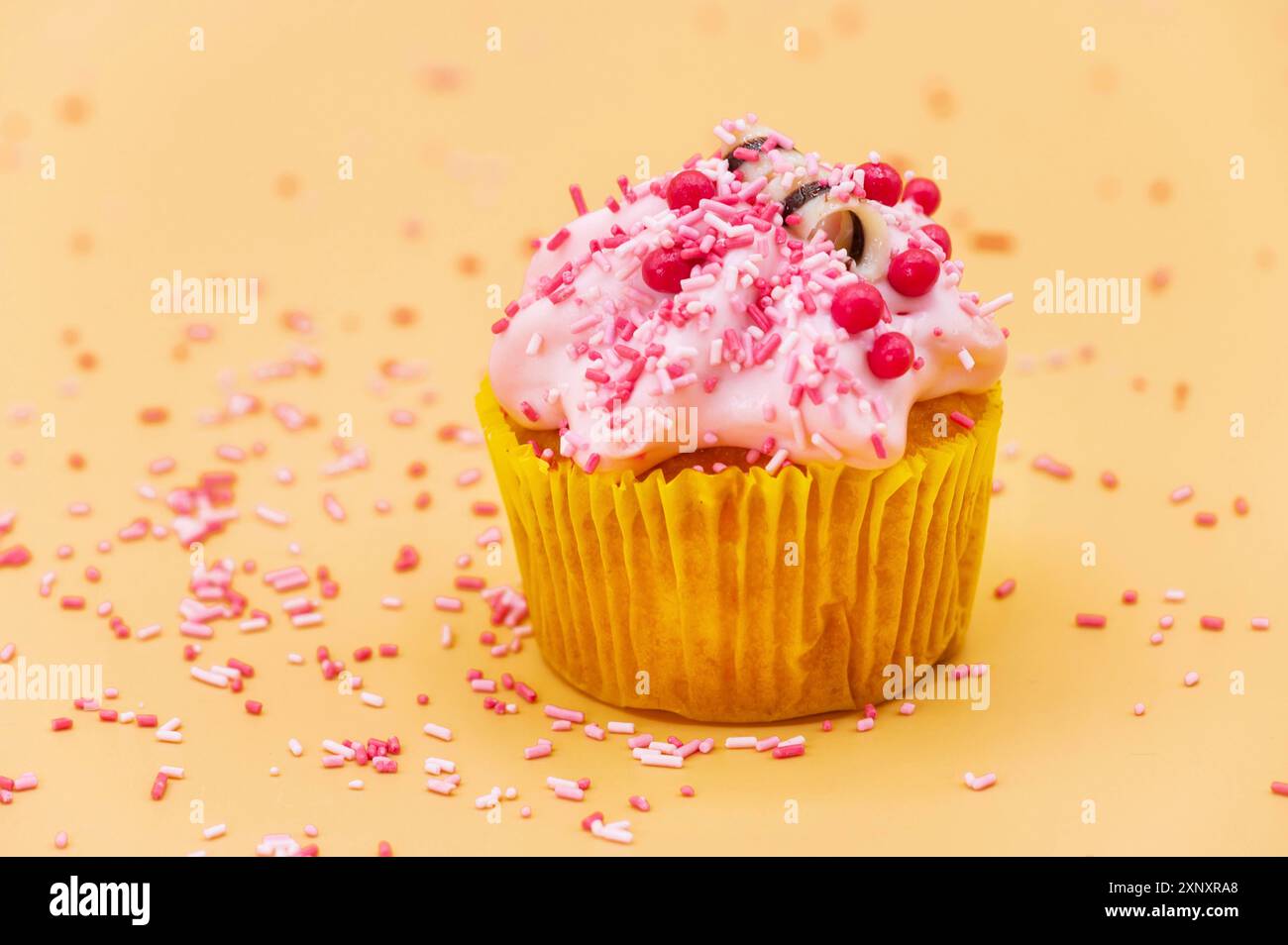 Einen Cupcake mit Sprinkles auf orangefarbenem Pastellhintergrund dekorieren Stockfoto