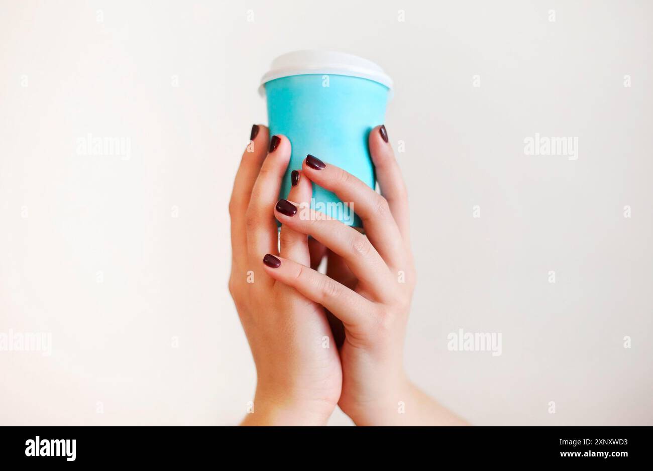 Ernte anonyme Frau in warmen Pullover mit dunkler Maniküre hält Einweg Tasse Kaffee während der Ruhepause am Holztisch Stockfoto