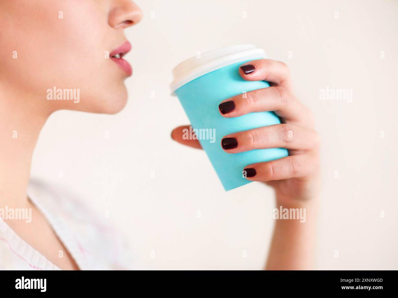Ernte anonyme Frau in warmen Pullover mit dunkler Maniküre hält Einweg Tasse Kaffee während der Ruhepause am Holztisch Stockfoto