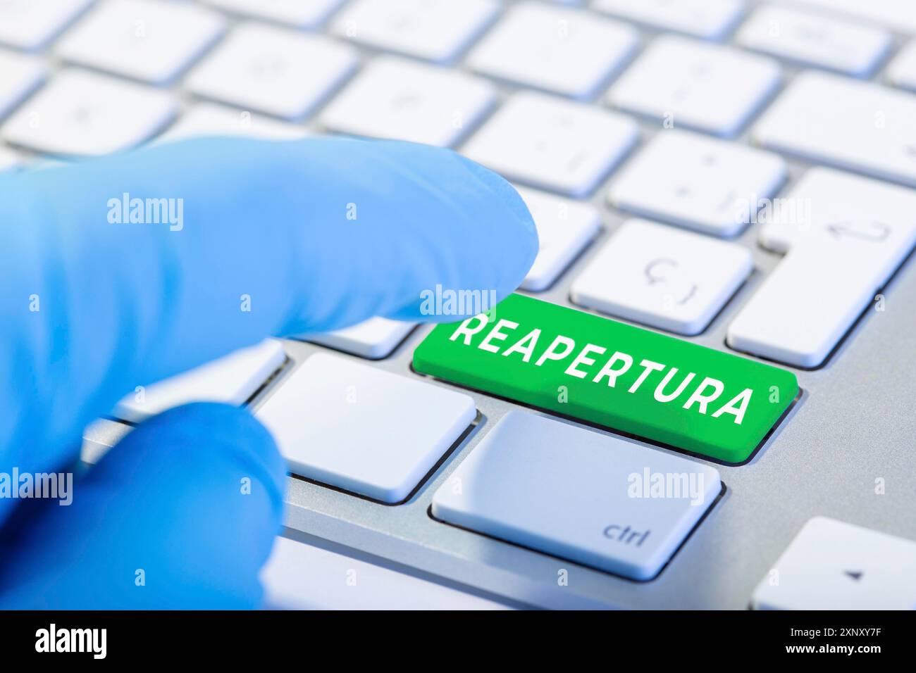 Wort in spanischer Sprache auf grüner Taste wieder öffnen Tastatur. Coronavirus Covid-19-Pandemie. Hand mit Schutzhandschuh bereit, um die Taste zu drücken Stockfoto