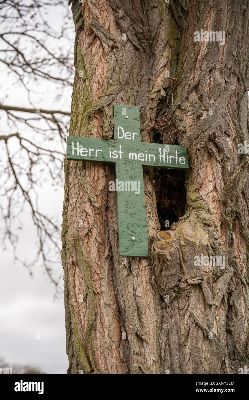 Religiöses Kreuz der herr ist mein Hirte, der darauf schreibt, hängt an einem Baum, bewölkter Tag, vertikaler Schuss Stockfoto