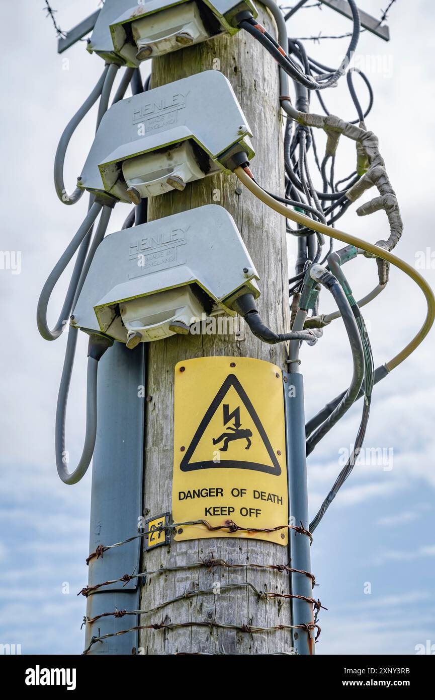 Alter hölzerner Strommast mit gelbem Warnschild und viel Kabel, vertikale Aufnahme Stockfoto