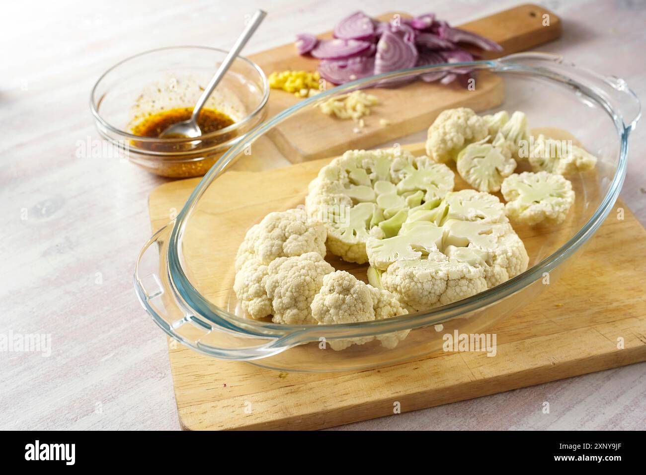 Rohe Blumenkohlscheiben in einem Glasauflauf, gehackte rote Zwiebeln und eine Gewürzmischung in Olivenöl, Zubereitung für gebackene Gemüsesteaks, Kopie Stockfoto