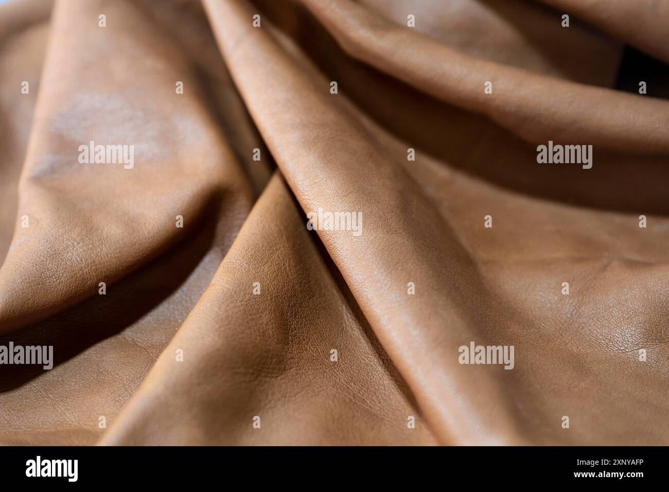 Weiches braunes Leder, das in Wellen liegt, für Möbel, Taschen oder Kleidung in einer Handwerkstatt verwendet wird, Vollformathintergrund, Kopierraum, ausgewählter Fokus Stockfoto