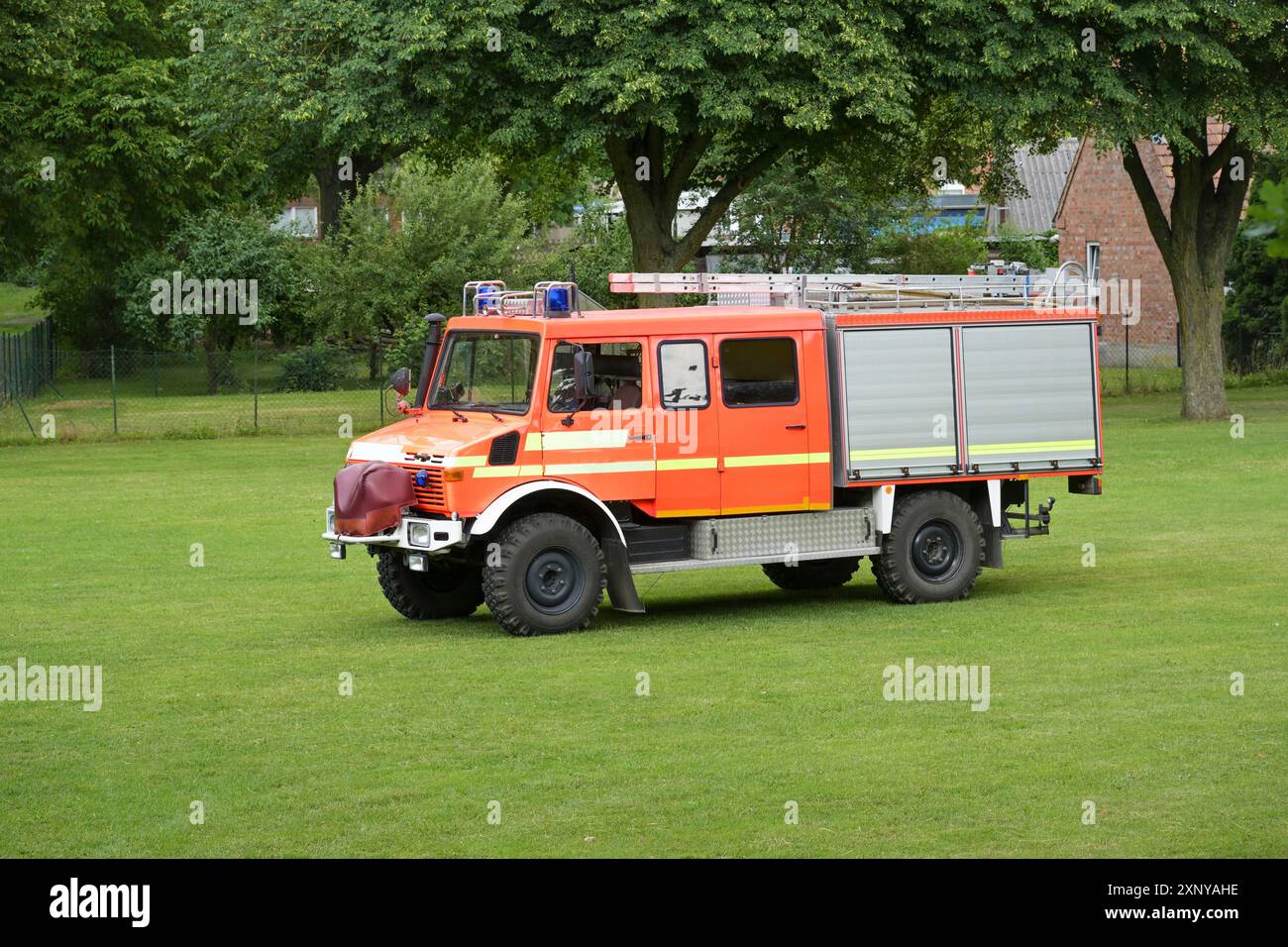 Deutsches Feuerwehrauto, rot-orangefarbener Lastwagen mit Leitern auf dem Dach und Ausrüstung für die Brandbekämpfung hinter Rollladentüren auf einer Wiese, Kopie Stockfoto