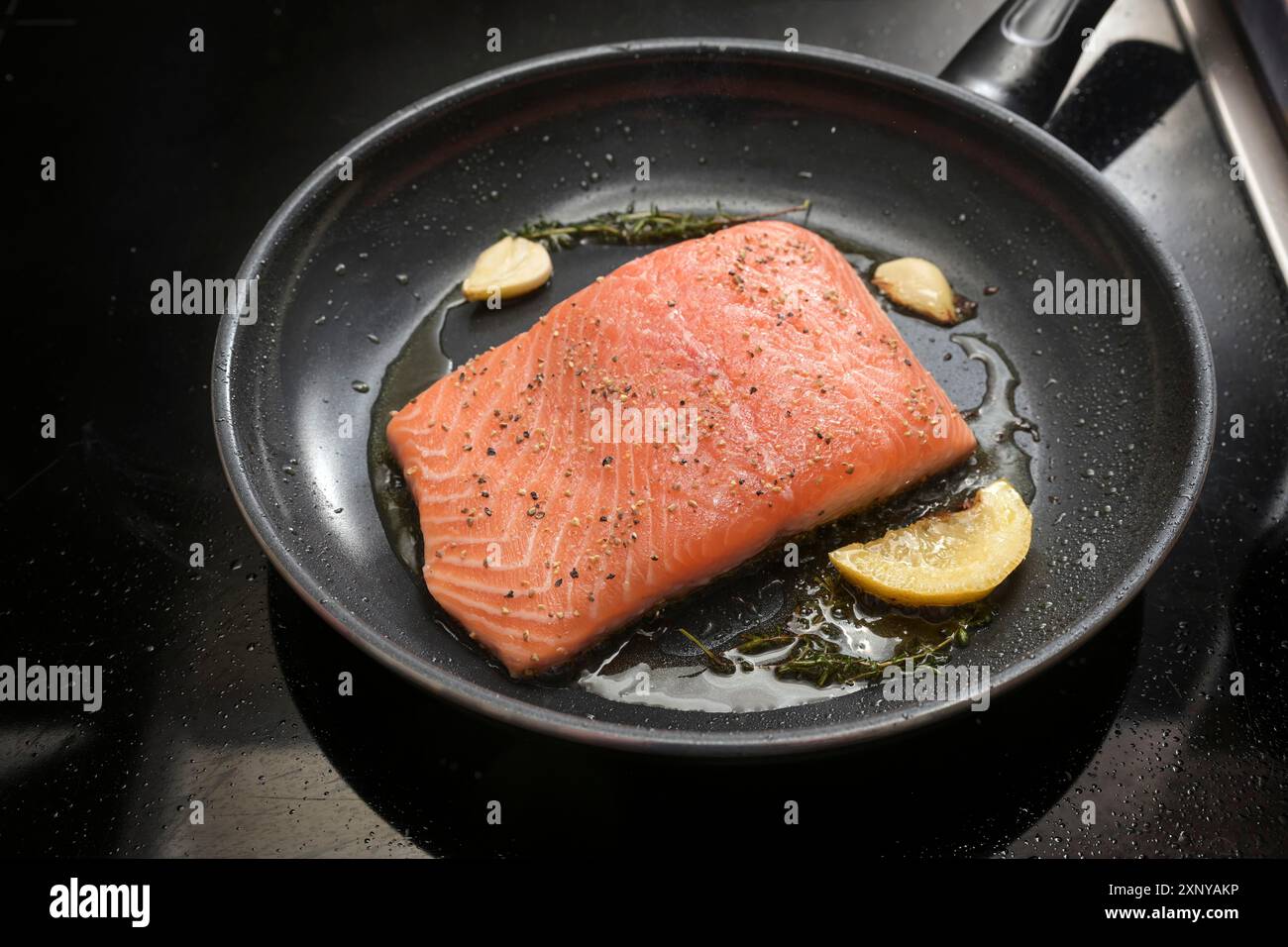 Frisches Lachsfilet wird auf der Haut mit Zitrone, Kräutern und Knoblauch in einer schwarzen Pfanne auf dem Herd gebraten, Kopierraum, ausgewählter Fokus, enge Tiefe Stockfoto