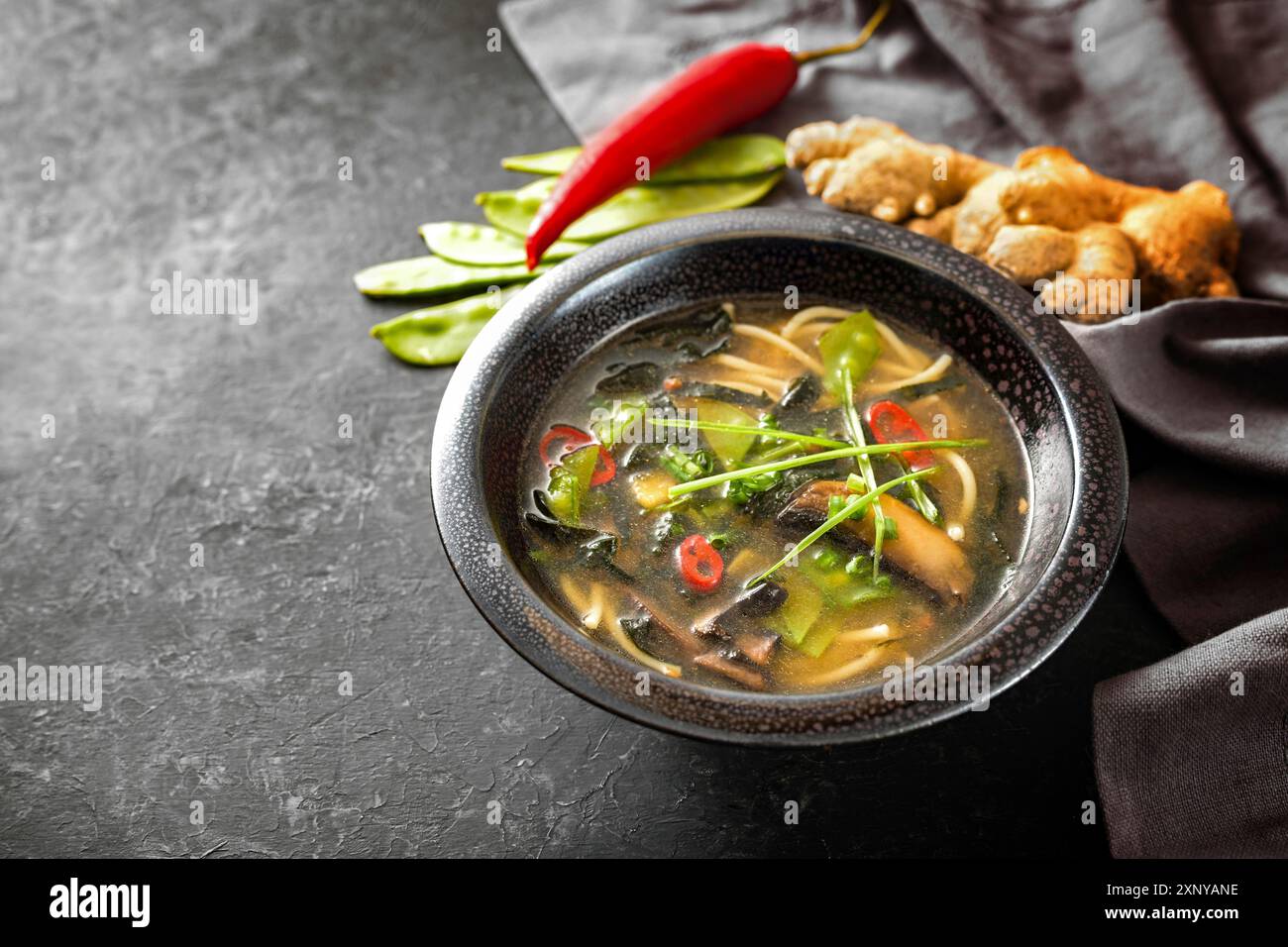 Asiatische Gemüsesuppe mit Nudeln, Pilzen, Zuckererbsen, Nori, Ingwer und Chili, traditionell mit Miso-Paste in einer schwarzen Keramikschale auf einem gewürzt Stockfoto