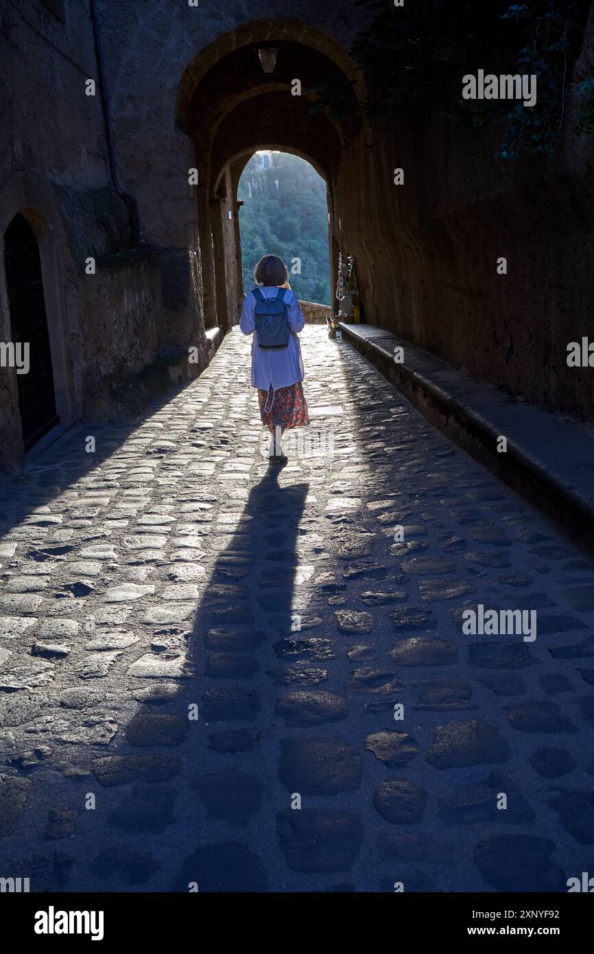 Mädchen auf einer Kopfsteinpflasterstraße mit einem Steintor in Bagnoregio, Italien Stockfoto