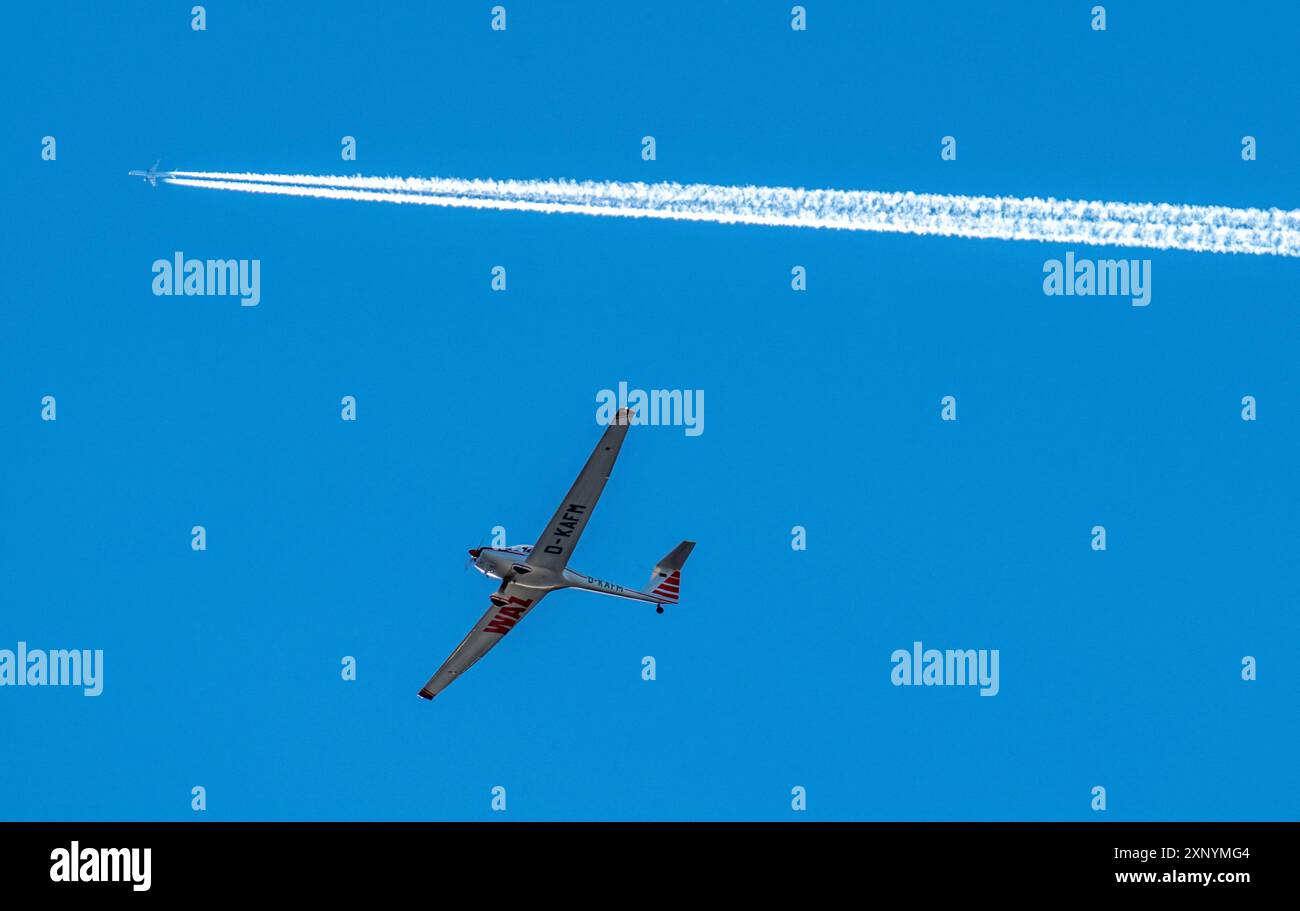 Zweimotoriger Jet, Passagierflugzeug, mit Kondensstreifen, am Himmel, unter einem motorisierten Segelflugzeug Stockfoto