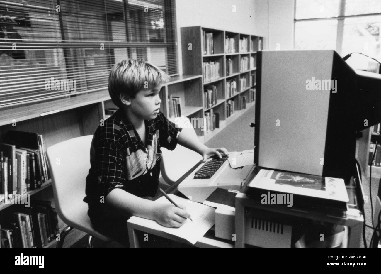 Austin Texas USA, 1990: Junge der vierten Klasse macht sich Notizen, während er Informationen auf einem Computer in der Schulbibliothek sucht. ©Bob Daemmrich Stockfoto
