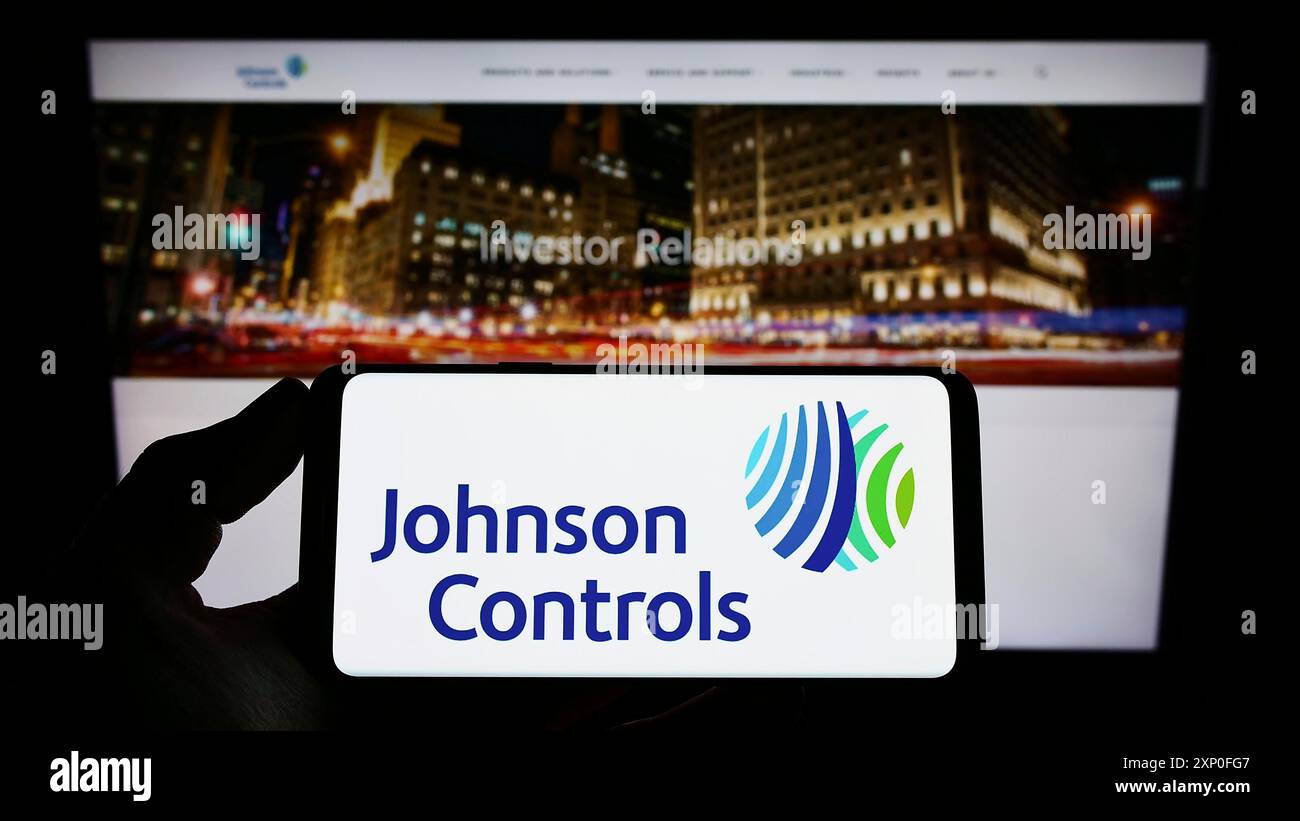 Stuttgart, Deutschland, 03.12.2022: Person, die ein Smartphone hält, mit dem Logo der Firma Johnson Controls International plc (JCI) auf dem Bildschirm davor Stockfoto
