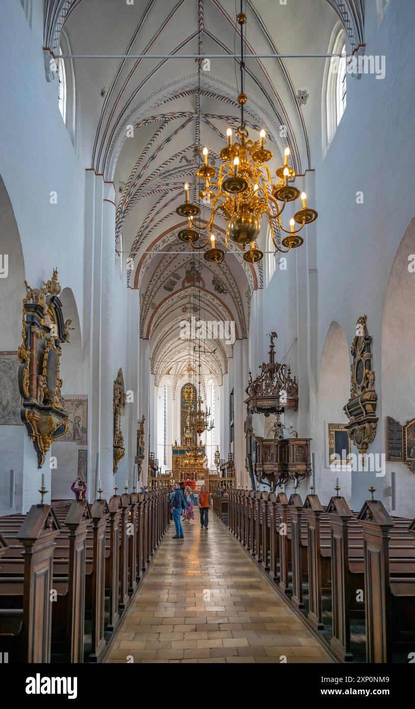 Drinnen in der Kathedrale von Aarhus, beleuchteter Kronleuchter, der auf dem Dach hängt, Holzbänke, Flur, Tourist im Hintergrund, vertikale Aufnahme Stockfoto
