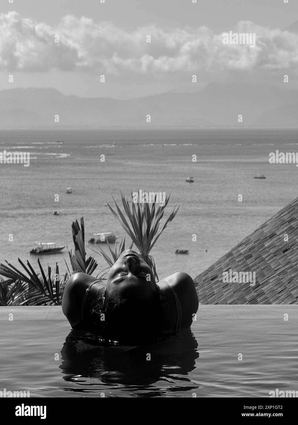 Eine Frau liegt in einem Pool mit dem Kopf im Wasser. Der Pool ist von einer üppigen grünen Pflanze umgeben Stockfoto