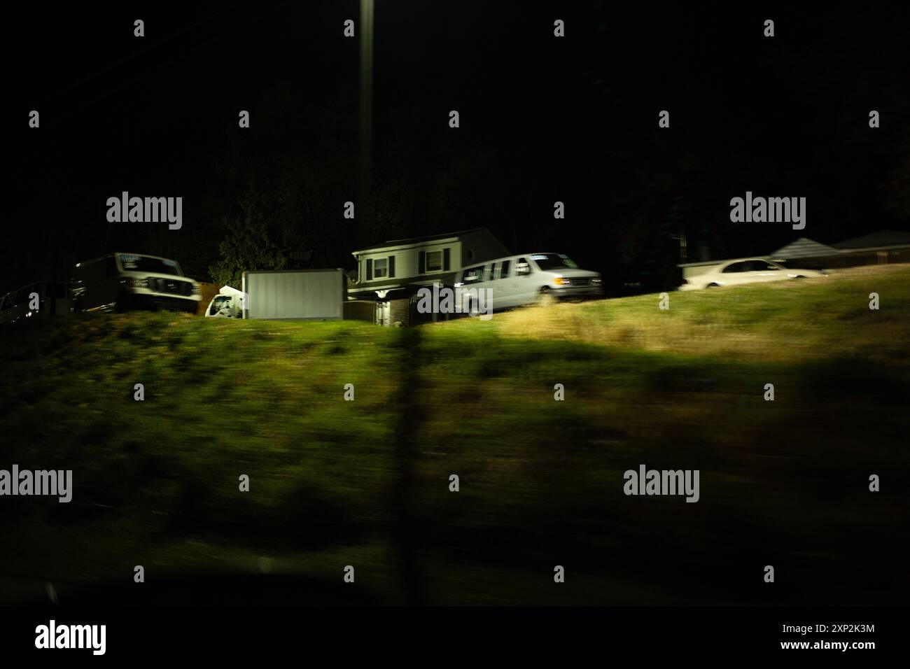 Vorstadtszene mit Häusern und geparkten Autos, die von einer Straßenlaterne beleuchtet werden, symbolisiert Ruhe und Stille einer Nacht in der Nachbarschaft. Stockfoto