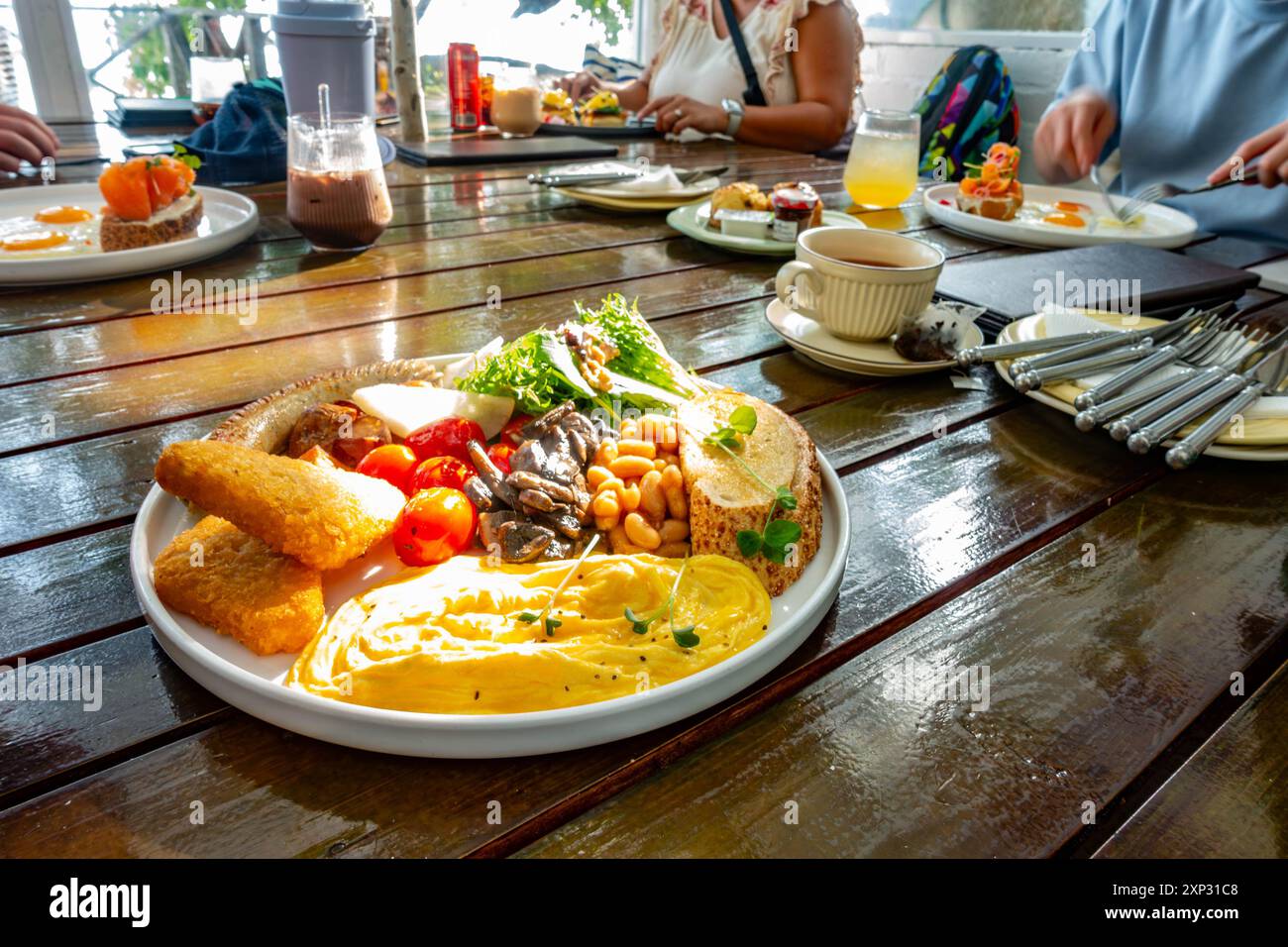 Ein Teller warmes Frühstück im Vordergrund und Familienfrühstück auf einem Holztisch im Hintergrund. Stockfoto