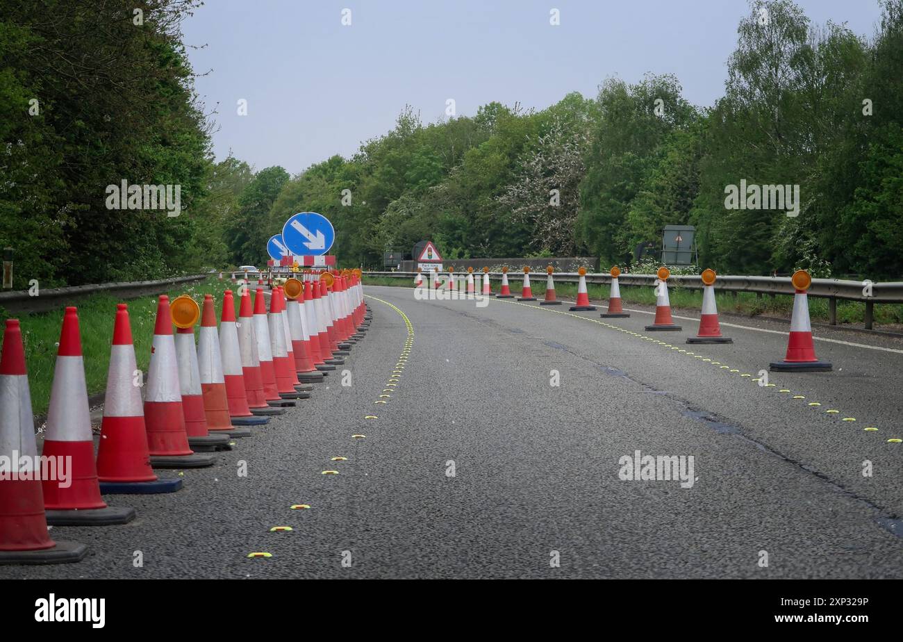 Verkehrskegel auf der A303-Hauptstraße filtern Fahrzeuge auf einer zweispurigen Fahrbahn an Baustellen in eine einspurige Spur. Stockfoto