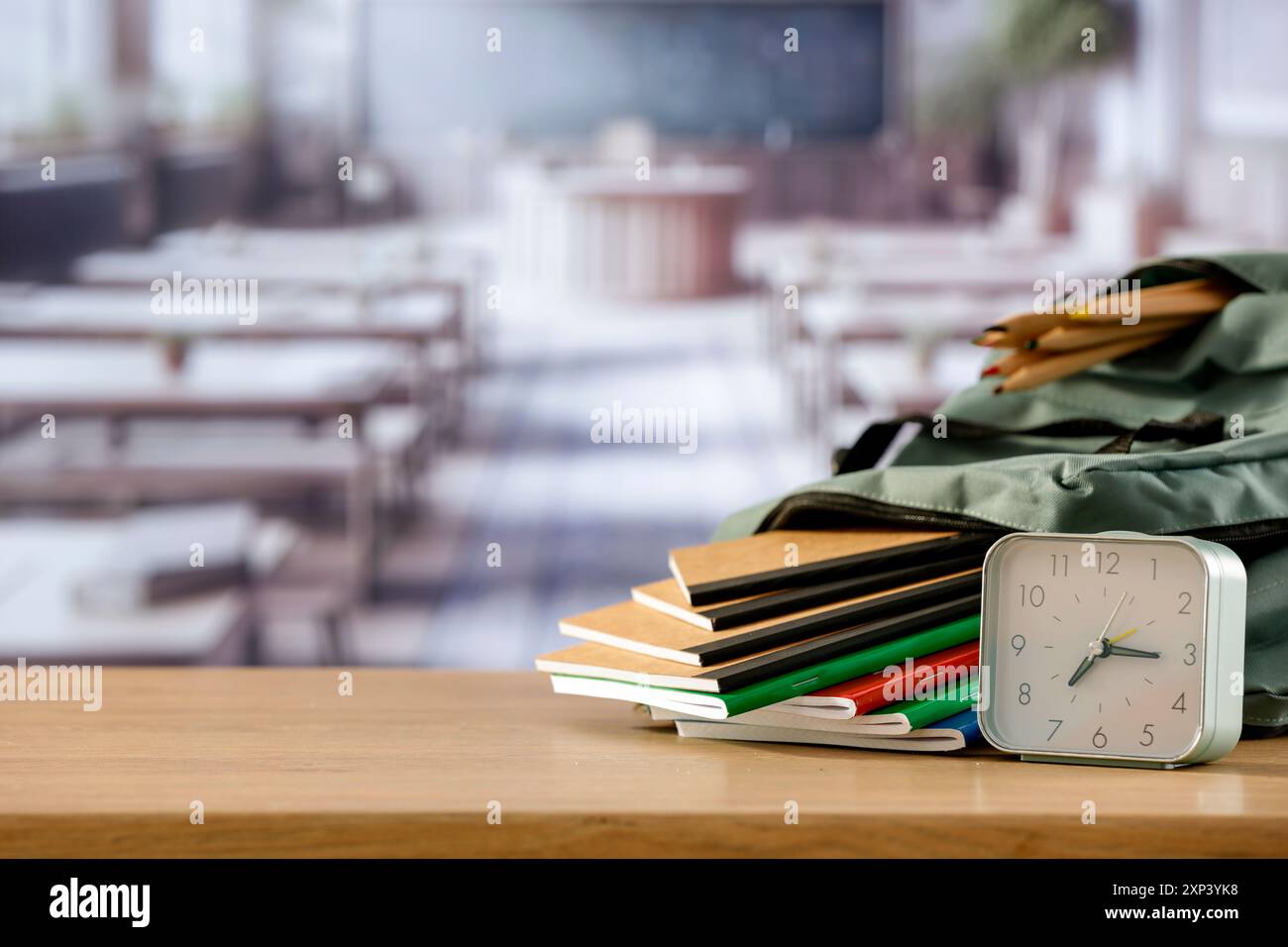 Schulsachen und Rucksack auf der Schulbank im Klassenzimmer. Verschwommener Hintergrund der Tafel an Wand und Fenster mit Sonnenlicht. Stockfoto