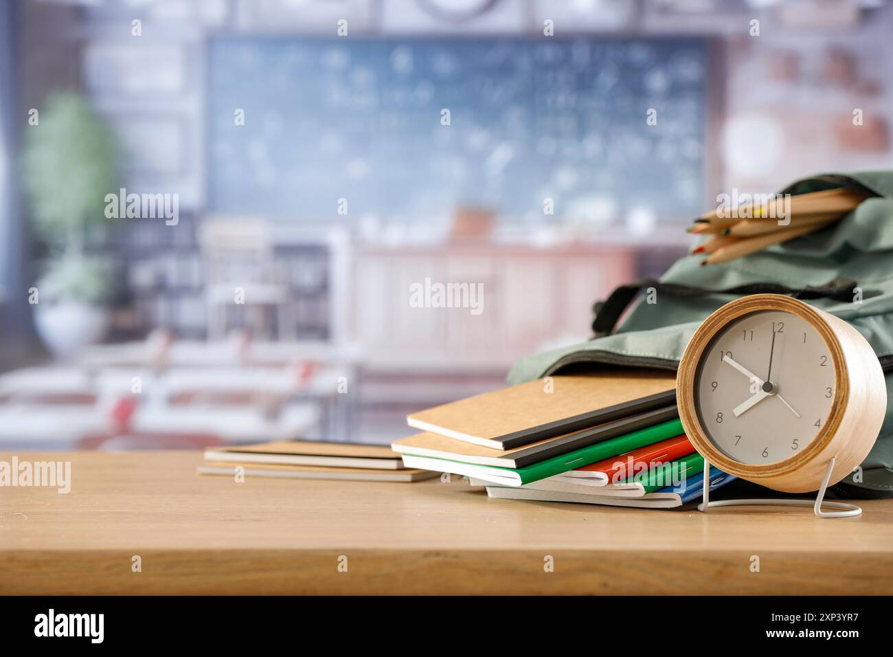 Schulsachen und Rucksack auf der Schulbank im Klassenzimmer. Verschwommener Hintergrund der Tafel an Wand und Fenster mit Sonnenlicht. Stockfoto