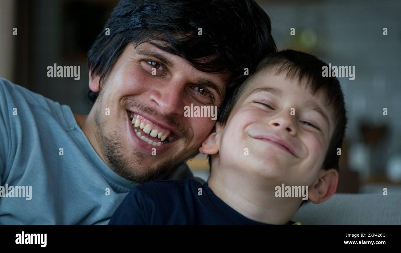 Ein fröhlicher Vater und Sohn, der glückliche Momente hat und warm in die Kamera lächelt. Familienbindung, Liebe und Zweisamkeit in einem gemütlichen Zuhause. Stockfoto