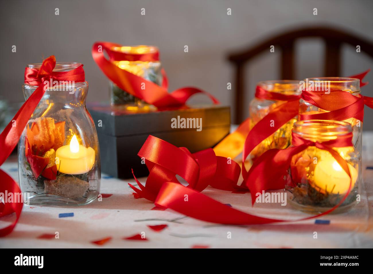 Warme Kerzen in Gläsern mit roten Bändern schaffen eine gemütliche festliche Atmosphäre. Stockfoto
