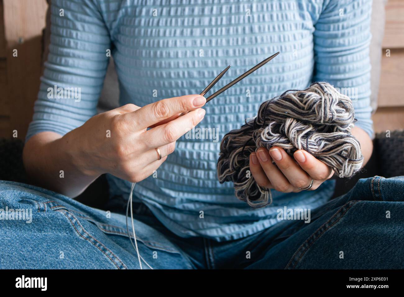 Frau in blauer Kleidung, die einen Ball aus grauem Garn und Stricknadeln hält. Mädchen, das mit gewebten Fäden und Nadeln in den Händen sitzt. Strickkonzept. Stockfoto