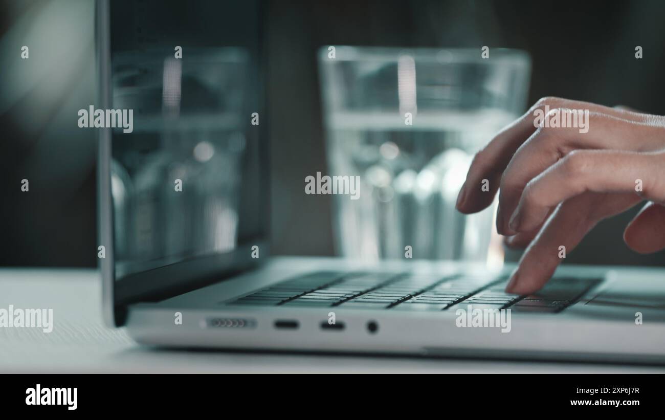 Weibliche Hände, die am Computer aus nächster Nähe tippen. Weibliche Benutzerin, die auf dem Schreibtisch der Notebook-Tastatur schreibt und online mit pc-Software-Apps arbeitet. Trinken Sie Wasser aus Glas, halten Sie die Gesundheit Gleichgewicht Hydration drinnen Stockfoto