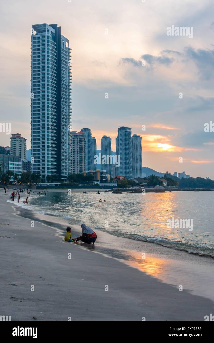 Ein Blick auf den Tanjing Tokong Strand in Penang, Malaysia bei Sonnenuntergang mit der Sonne, die orange im Meer reflektiert, mit einer Skyline der Stadt im Hintergrund. Stockfoto