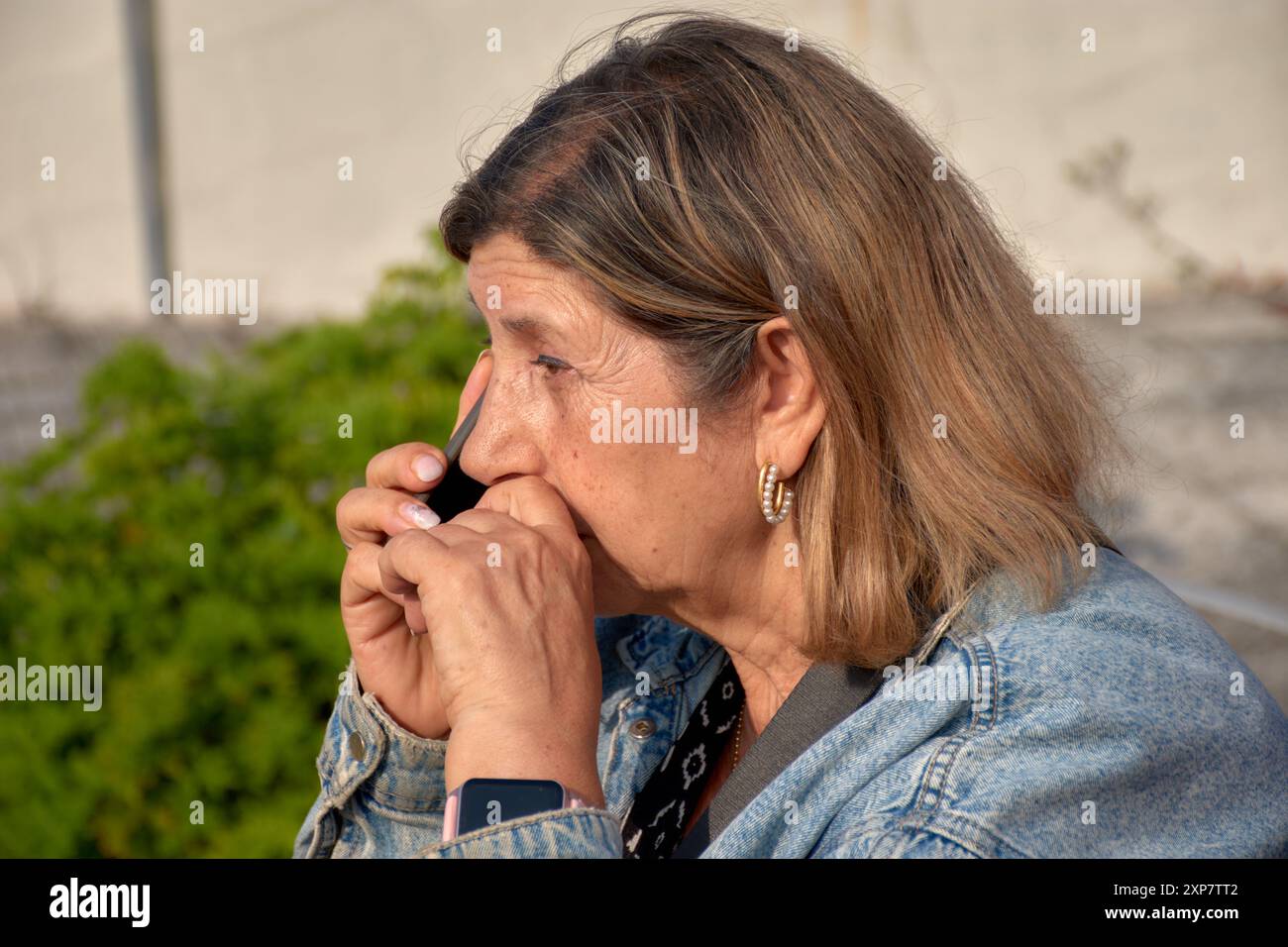 Eine ältere Frau sitzt und spricht mit einem ernsten Gesichtsausdruck auf ihrem Handy. Ihr fokussierter Blick deutet auf eine wichtige oder besorgniserregende Co hin Stockfoto