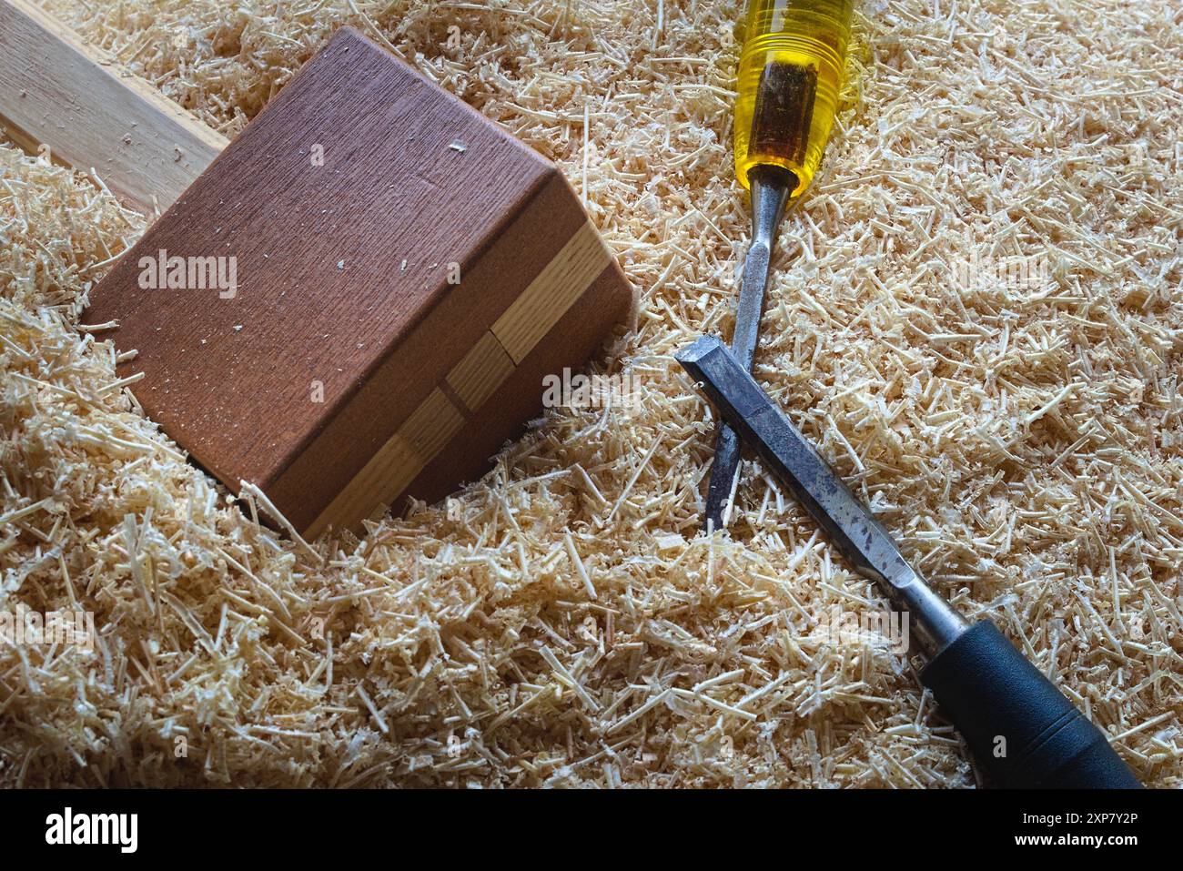 Ein handgefertigter Holzhammer und Meißel, die in Holzspänen in einer Holzwerkstatt sitzen. Stockfoto