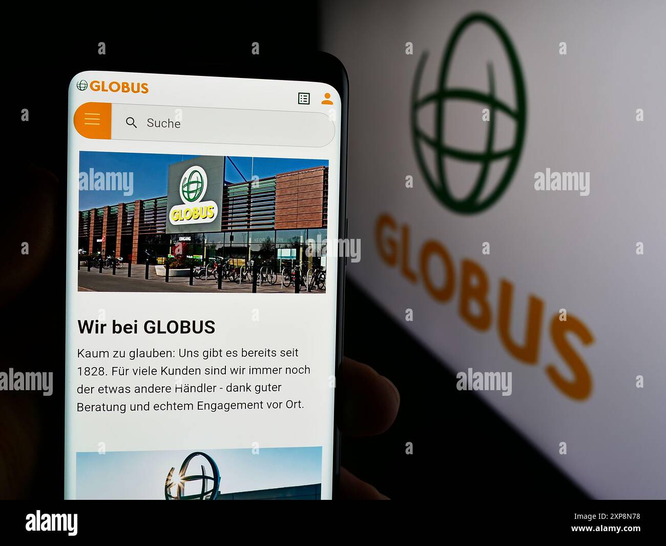 Person mit Smartphone und Webseite der deutschen Einzelhandelsgesellschaft Globus Holding GmbH Co. KG vor dem Logo. Konzentrieren Sie sich auf die Mitte des Telefondisplays. Stockfoto