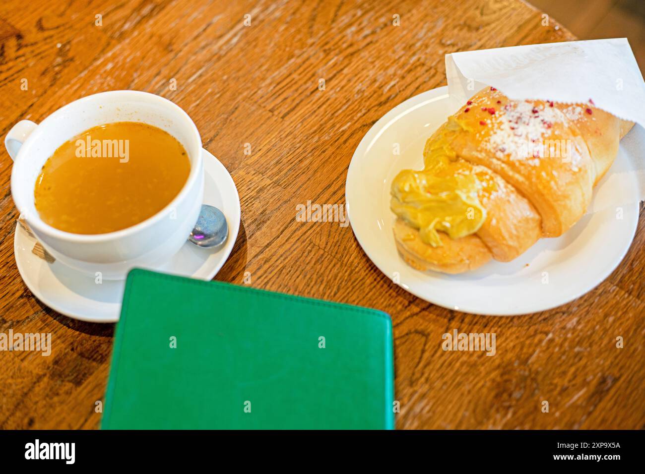 Heißes Croissant mit Pistaziencreme mit Tee und einem Notizbuch auf dem Tisch. Zurück zur Schule. Snack Stockfoto