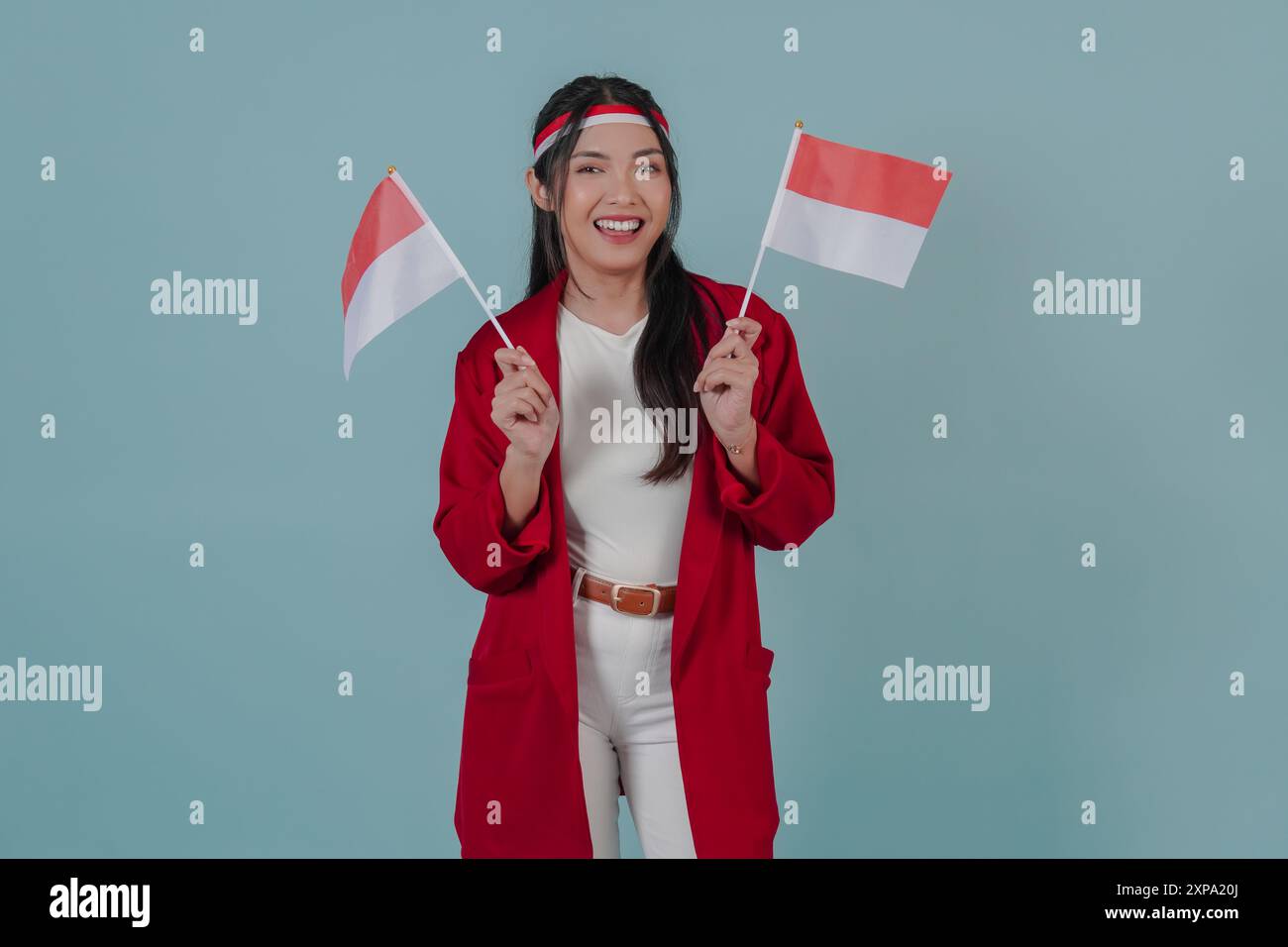 Eine glückliche indonesische Frau, die einen roten Mantel und eine weiße Hose trägt, hebt zwei Fahnen, während sie lächelt. Indonesien Unabhängigkeitstag Konzept. Stockfoto