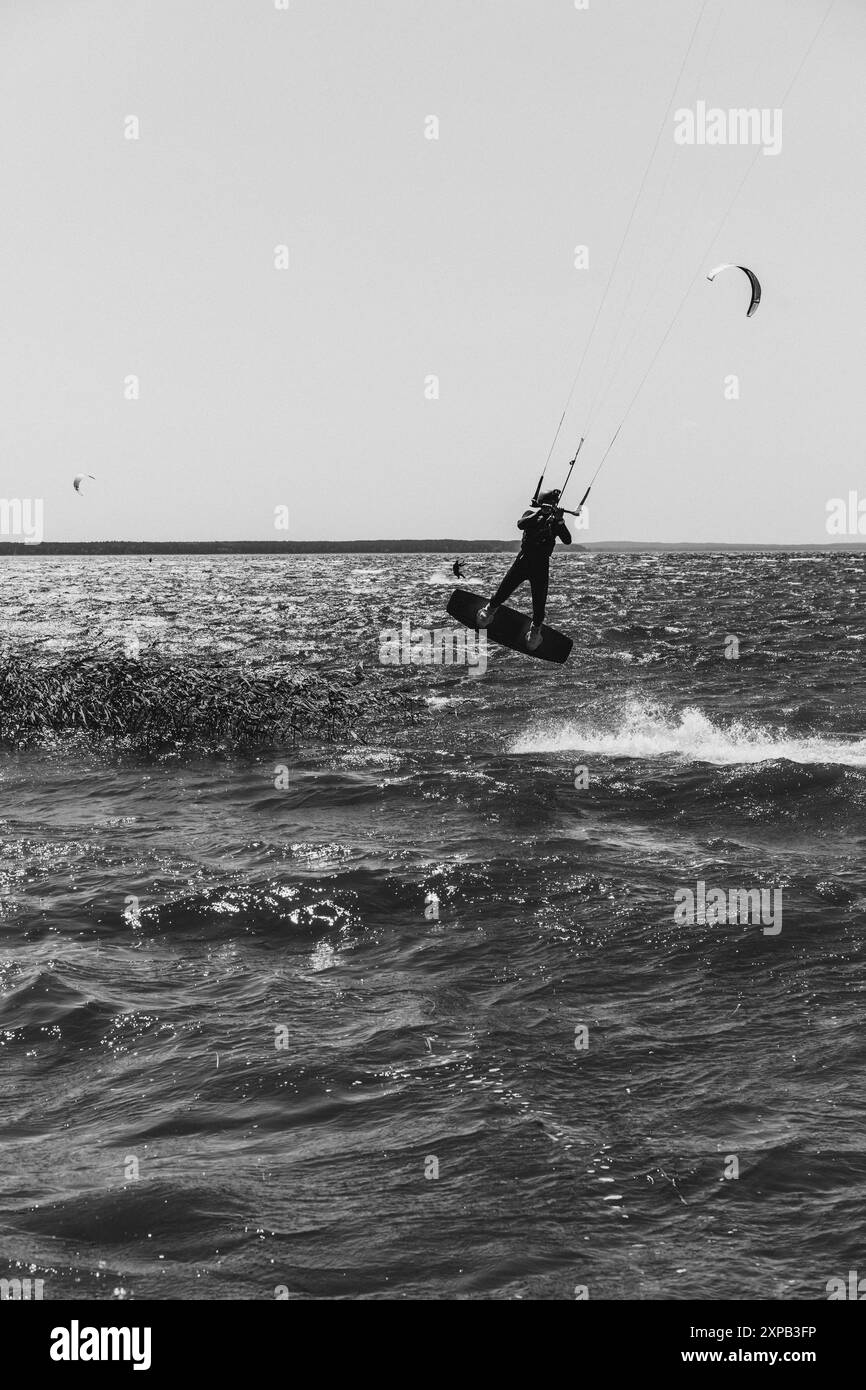 Ein Mann macht Tricks mit seinem Brett und übt Kitesurf-Sprung in die Luft. Stockfoto