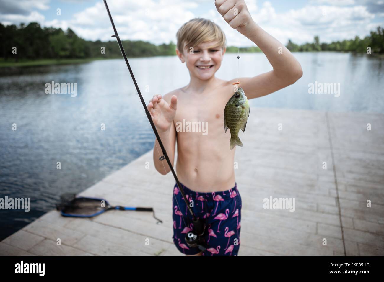 Junge am Dock lächelt mit Blaubarschfischen, die in der Schlange gefangen werden Stockfoto