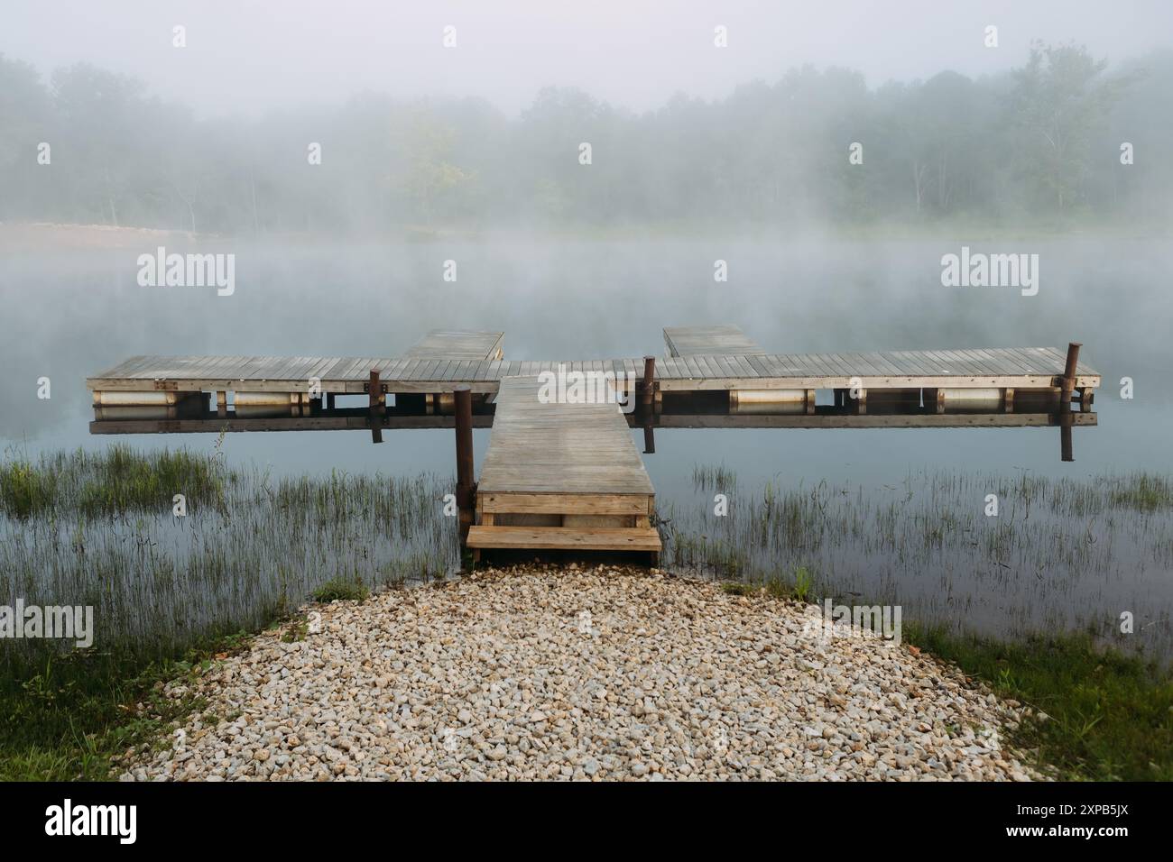 Am frühen Morgen hängt der Nebel über dem hölzernen Dock am Seeufer Stockfoto