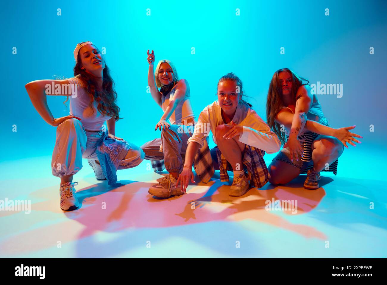Freunde in lässigen Outfits posieren energisch unter farbenfroher Beleuchtung und fangen das Wesen des modernen Tanzes in Neonlicht vor hellblauem Hintergrund ein Stockfoto