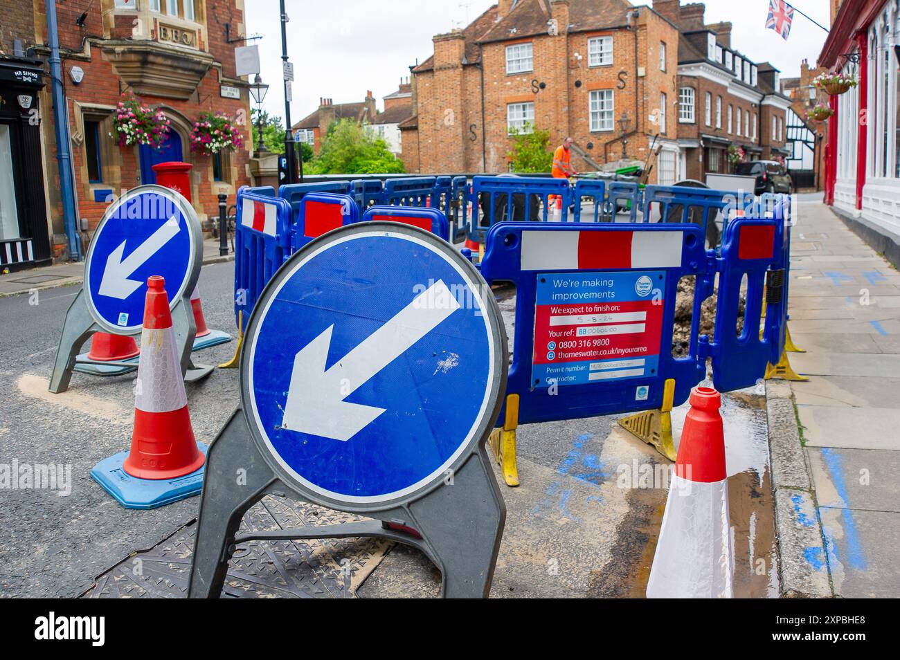 Eton, Windsor, Berkshire, Großbritannien. August 2024. Thames Water repariert eine Wasserleitung in der Eton High Street, Windsor, Berkshire. In der Zwischenzeit verbleiben Wasser- und Schlammrückstände auf der Straße. Die finanzielle Lage von Themse Water ist nach wie vor besorgniserregend. Es wird jetzt noch schwieriger für Thames Water sein, Geld zu leihen, da die führende Ratingagentur Moody's ihre Schulden auf "Junk"-Status herabgestuft hat. Es wurde gehofft, dass Keir Starmer die Themse renationalisieren würde, aber es wurde berichtet, dass er dies nicht tun wird. Kredit: Maureen McLean/Alamy Stockfoto