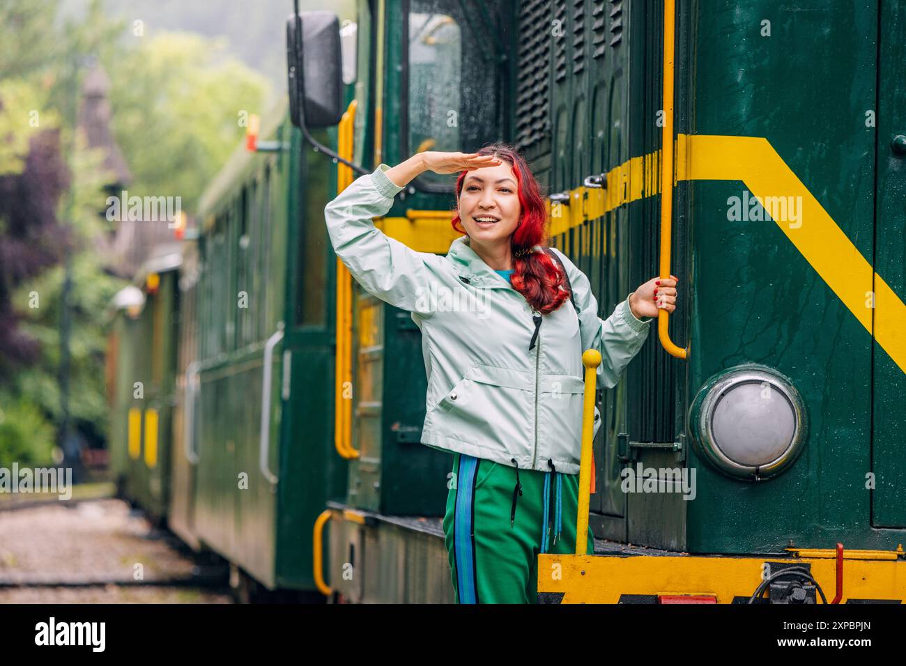 Passagiermädchen in lässiger Kleidung, Ankunft am historischen Bahnhof Mokra Gora, begrüßt vom Charme des alten Lokomotivzuges und des alten Wagens. Stockfoto